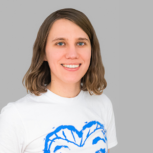 A caucasian woman in her 20s with blue eyes and shoulder-length brown hair, wearing a white t-shirt with a blue heart on it. 